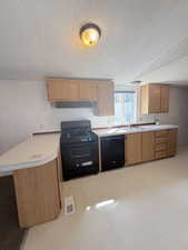 Kitchen featuring black appliances, light countertops, a textured ceiling, under cabinet range hood, and light flooring