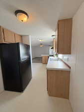 Kitchen featuring freestanding refrigerator, light countertops, light flooring, a textured ceiling, and a peninsula