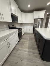 Kitchen with stainless steel appliances, white cabinets, light stone countertops, dark cabinets, and light wood-style floors
