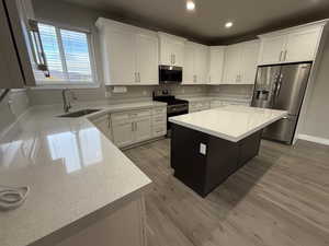 Kitchen featuring white cabinets, appliances with stainless steel finishes, a kitchen island, light stone countertops, and recessed lighting