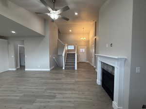 Unfurnished living room featuring stairs, high vaulted ceiling, light wood-style floors, a premium fireplace, and a ceiling fan