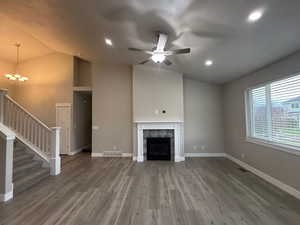 Unfurnished living room featuring lofted ceiling, ceiling fan, light wood-style floors, stairway, and a tiled fireplace