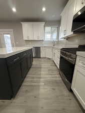 Kitchen featuring stainless steel appliances, white cabinets, dark cabinets, recessed lighting, and light stone countertops