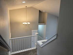 Staircase with a textured ceiling, carpet, a chandelier, and high vaulted ceiling