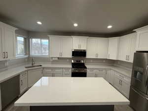 Kitchen featuring stainless steel appliances, light stone countertops, a kitchen island, white cabinetry, and recessed lighting