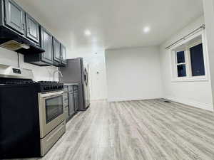 Kitchen with stainless steel appliances, light wood finished floors, under cabinet range hood, dark cabinets, and open floor plan
