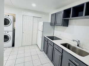 Kitchen with open shelves, light tile patterned floors, stacked washer / dryer, and gray cabinets