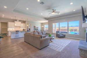 Living room with ceiling fan, a raised ceiling, recessed lighting, a chandelier, and a glass covered fireplace