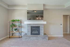 Unfurnished living room featuring a fireplace, light colored carpet, and a ceiling fan