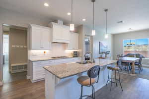 Kitchen with plenty of natural light, white cabinets, light stone countertops, hanging light fixtures, and recessed lighting