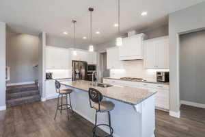 Kitchen with a kitchen bar, decorative backsplash, white cabinetry, appliances with stainless steel finishes, and a center island with sink
