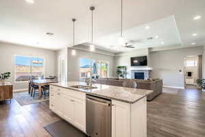 Kitchen featuring white cabinets, a brick fireplace, light stone countertops, dishwasher, and pendant lighting