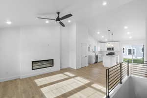 Unfurnished living room with light wood-style flooring, a glass covered fireplace, recessed lighting, high vaulted ceiling, and ceiling fan