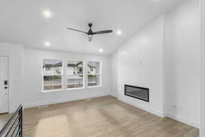Unfurnished living room featuring a glass covered fireplace, light wood-style flooring, recessed lighting, a ceiling fan, and lofted ceiling