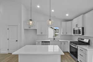 Kitchen with stainless steel appliances, lofted ceiling, light wood-type flooring, white cabinetry, and pendant lighting