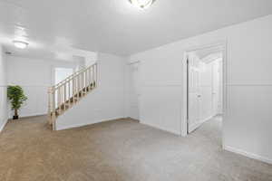 Unfurnished room featuring a wainscoted wall, a textured ceiling, light colored carpet, and stairway
