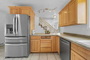 Kitchen with stainless steel appliances, a textured ceiling, light tile patterned flooring, and light countertops