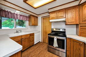 Kitchen featuring stainless steel electric stove, brown cabinetry, wood finished floors, light countertops, and crown molding