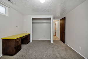 Unfurnished bedroom with light carpet, a textured ceiling, an office area, and a closet