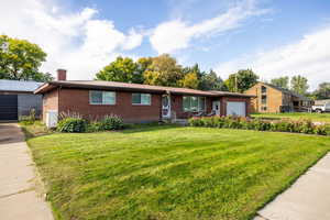 View of front of property featuring brick siding, a garage, a chimney, and a front lawn