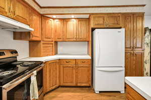 Kitchen featuring stainless steel electric range oven, freestanding refrigerator, light countertops, brown cabinetry, and crown molding