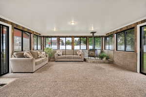 Sunroom / solarium with a wood stove, plenty of natural light, carpet floors, wooden walls, and crown molding