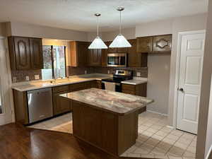 Kitchen with appliances with stainless steel finishes, a textured ceiling, decorative light fixtures, light tile patterned floors, and tasteful backsplash