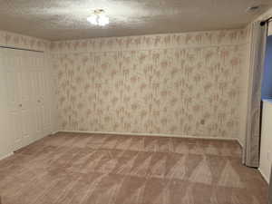 Unfurnished bedroom with a textured ceiling, carpet floors, wallpapered walls, and a closet