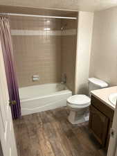 Bathroom with shower / bathtub combination with curtain, dark wood-type flooring, vanity, wallpapered walls, and a textured ceiling