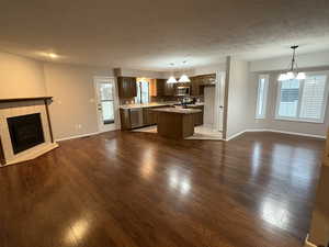 Kitchen featuring open floor plan, hanging light fixtures, dark wood-type flooring, and a textured ceiling