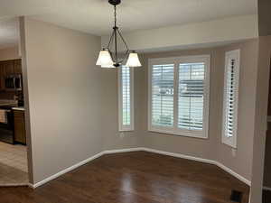 Unfurnished dining area with a textured ceiling, dark wood-style flooring, and a chandelier