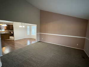 Spare room with high vaulted ceiling, a chandelier, dark colored carpet, and dark wood-style floors