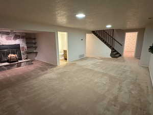 Unfurnished living room featuring a textured ceiling, carpet floors, a stone fireplace, and stairway