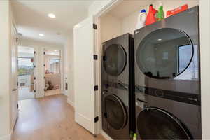 Laundry room featuring light wood finished floors, recessed lighting, and stacked washer and clothes dryer