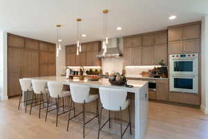 Kitchen featuring a breakfast bar area, brown cabinets, double oven, a large island, and wall chimney exhaust hood