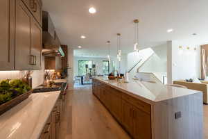 Kitchen with light wood finished floors, open floor plan, light stone countertops, tasteful backsplash, and wall chimney exhaust hood