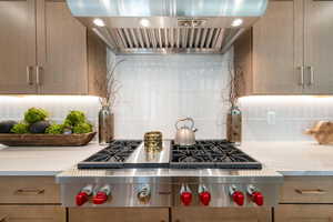 Kitchen featuring range hood, tasteful backsplash, stainless steel gas cooktop, light stone counters, and light brown cabinetry