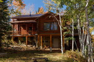 Rear view of house featuring log siding, a metal roof, and stone siding