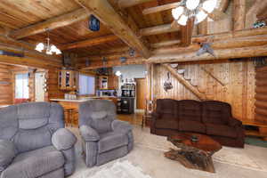 Living area with rustic walls, stairs, a wood ceiling with exposed beams, ceiling fan, and a chandelier