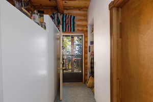 Hall featuring log walls, dark colored carpet, and a wooden ceiling with exposed beams