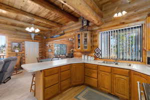 Kitchen featuring open floor plan, a kitchen breakfast bar, glass insert cabinets, a wooden ceiling with exposed beams, and a chandelier
