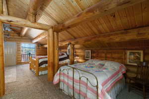 Carpeted bedroom with rustic walls and a wooden ceiling with exposed beams