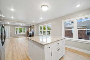 Kitchen with white cabinetry, stainless steel fridge, a center island, light stone countertops, and light wood-style flooring