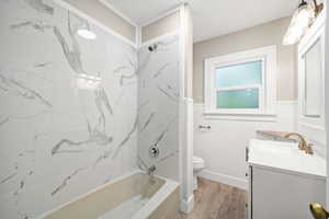 Full bath with a combined bath / shower with marble appearance, vanity, light wood-style floors, and a wainscoted wall