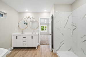 Full bathroom featuring double vanity, a marble finish shower, light wood-type flooring, a soaking tub, and recessed lighting