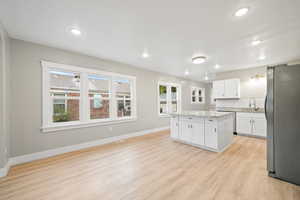 Kitchen featuring white cabinetry, freestanding refrigerator, a kitchen island, light wood-style floors, and recessed lighting