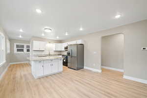 Kitchen featuring white cabinets, appliances with stainless steel finishes, backsplash, a center island, and arched walkways