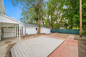 Composite Wood and paver deck featuring a Covered patio, a fenced backyard, mature tree, Garage and attached storage shed.