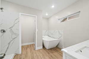 Full bath with a soaking tub, vanity, a marble finish shower, light wood-style flooring, and recessed lighting