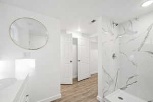 Full bathroom featuring vanity, a marble finish shower, and light wood-style floors